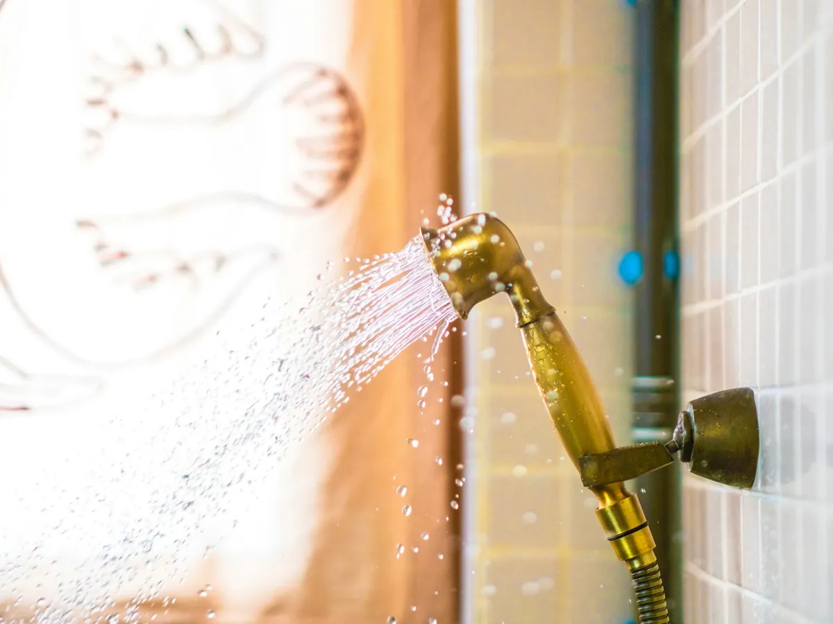 Hand shower spraying water against a tiled wall